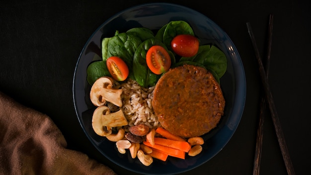 Draufsicht auf einen Teller mit leckerem veganem Sojaprotein-Kotelett-Burger mit braunem Reis und Gemüse