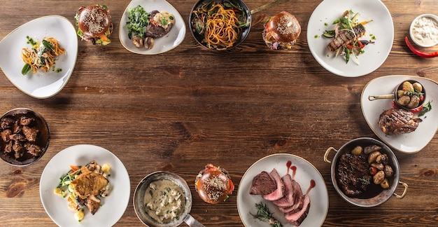 Draufsicht auf einen Tisch voller verschiedener Mahlzeiten für Vegetarier und Fleischesser, die im Kreis serviert werden.
