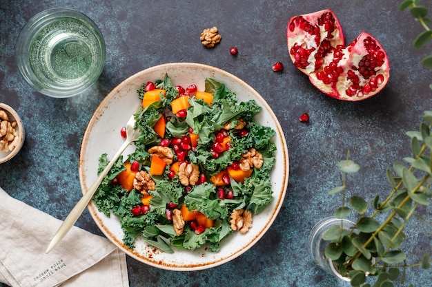 Draufsicht auf einen veganen frischen Salat, der aus rohem Gemüse wie Persimmon Kale Granatapfelsamen und Walnuss auf blauem Hintergrund hergestellt wird Gesundes Ernährungs- und Lifestyle-Konzept flach gelegt