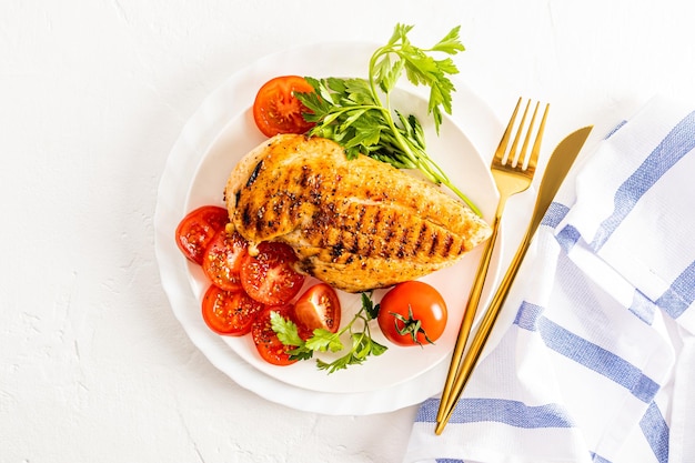 Draufsicht auf einen weißen Servierteller mit gegrilltem Hähnchenbrustfilet mit Kirschtomatenscheiben und Petersilie weißer Hintergrund ein Kopierraum