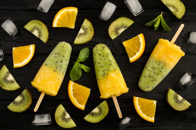 Draufsicht auf Eis am Stiel mit Kiwi und Orangenfrucht auf dem schwarzen Holztisch. Nahansicht.