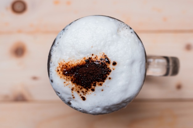 Draufsicht auf Eiskaffeeschaum in Tasse und Kaffeepulver mit Kaffeebohnen auf Holzboden.