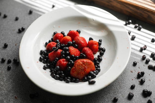Draufsicht auf Erdbeeren und schwarze Johannisbeeren in einem weißen Teller am Fenster. Gesundes Ernährungskonzept