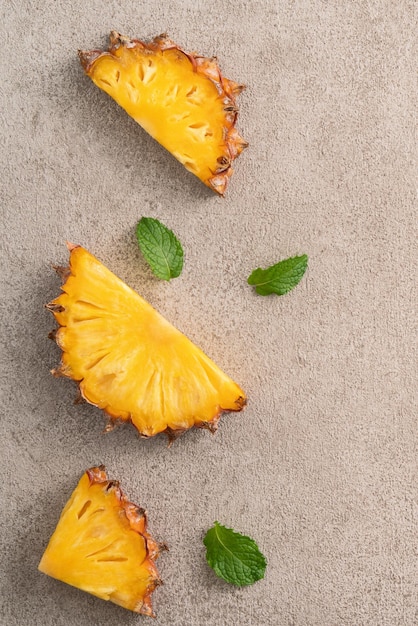 Draufsicht auf frisch geschnittene Ananas mit tropischen Blättern auf grauem Tischhintergrund