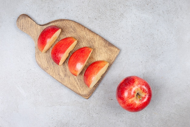 Draufsicht auf frische apfelscheiben auf holzschneidebrett und ganzen apfel auf grauer oberfläche.