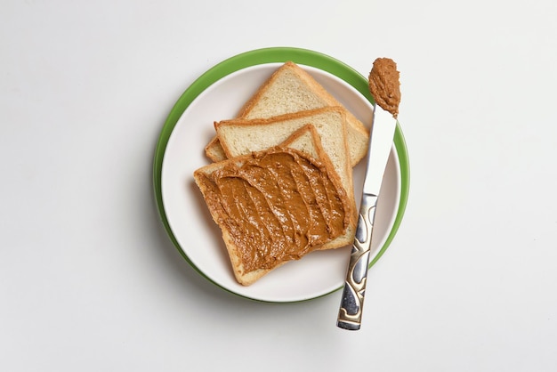 Draufsicht auf frische Toasts auf dem Teller, die mit leckerer Erdnussbutter auf der weißen Oberfläche gebuttert sind