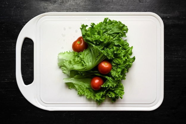 Draufsicht auf frischen Salat und Tomaten auf weißem Schneidebrett