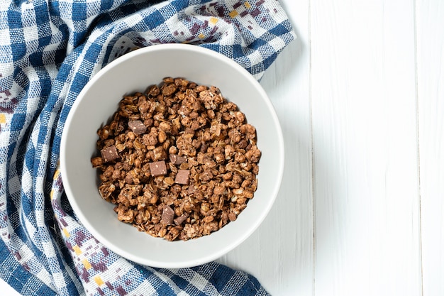 Draufsicht auf frisches Schokoladenmüsli in grauer Schüssel mit blauem Stoff auf weißem hölzernem Hintergrund. Speicherplatz kopieren. Gesundes und leckeres Frühstück. Veganes Essen. Lebensmittel Foto Hintergrund