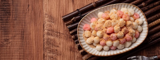 Draufsicht auf frittierten roten und weißen Tangyuan (Tang Yuan, klebrige Reisknödelbällchen) mit Erdnusspulver auf Holztischhintergrund für Wintersonnenwende-Festivalessen.