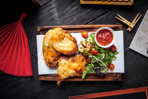 Draufsicht auf gebratenes Huhn mit Soße und Grün auf dem Holzbrett