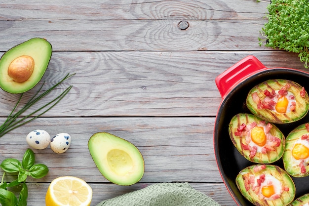 Draufsicht auf gegrillte Avocadoboote mit Speck und Ei, flach auf Holz liegend