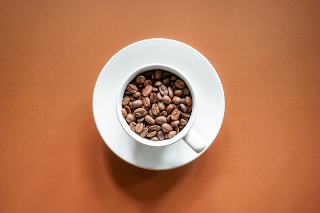 Draufsicht auf geröstete Kaffeebohnen in weißer Kaffeetasse mit braunem Hintergrund