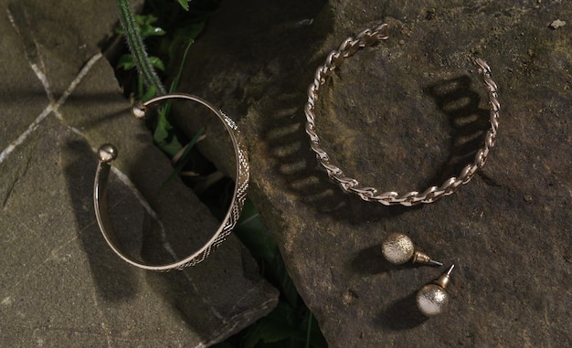 Draufsicht auf glänzende goldene kettenförmige Armbänder und Ohrringe paaren sich auf Naturstein im Freien