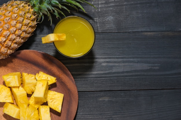 Draufsicht auf Gläser Ananassaft und Ananasfrucht auf einem schwarzen Holztisch