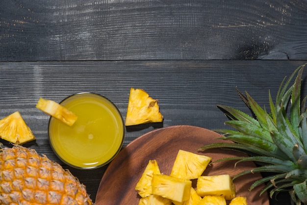 Draufsicht auf Gläser Ananassaft und Ananasfrucht auf einem schwarzen Holztisch