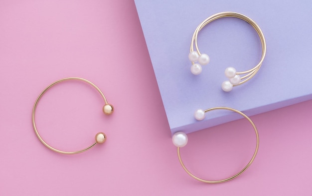 Draufsicht auf goldene Armbänder mit Perlen auf rosa und violettem Papierhintergrund mit Kopierraum