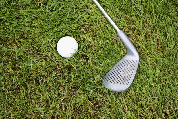 Draufsicht auf Golfball und Schläger, die auf frischer grüner Rasenplatzausrüstung für Profis liegen
