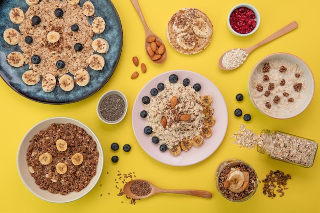 Draufsicht auf Haferflocken mit Bananen-Schwarzdorn-Mandel-Flachs in Tellern und Schalen mit Bananen-Knäckebrot-Snack und Bananen-Walnuss-Smoothie-Chia-Samen auf gelbem Hintergrund