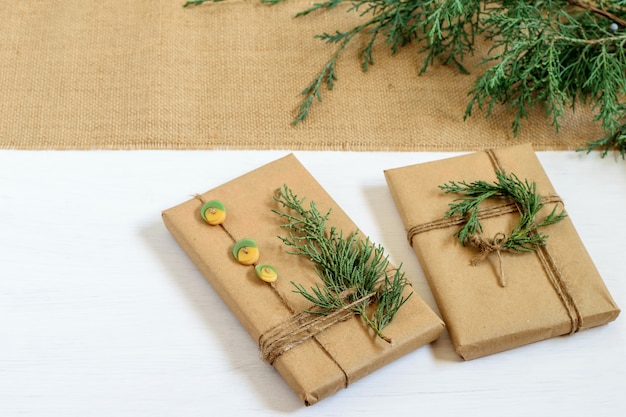 Draufsicht auf handgemachte Weihnachtsgeschenke, eingewickelt in recyceltes Bastelpapier, verziert mit Thujazweigen und Knöpfen.