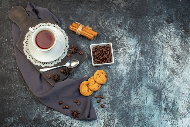 Draufsicht auf hausgemachte Kekse, Zimtlimetten und eine Tasse Tee auf Holzbrett auf Eishintergrund