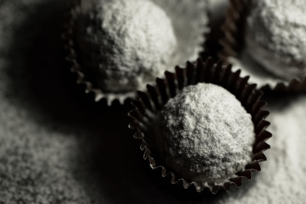 Draufsicht auf hausgemachte Schokoladenbonbons, die mit Puderzucker auf dunklem Hintergrund bestreut sind