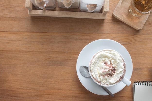 Draufsicht auf heiße Schokolade mit Schlagsahne auf hölzernen Schreibtisch im Café