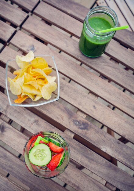 Draufsicht auf infundierte Fruchtwassercocktails und grüne Gemüsesmoothies über einem Holztisch im Freien. Gesundes Bio-Sommergetränkekonzept.