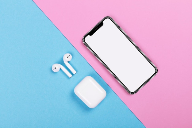 Draufsicht auf iPhone und Apple AirPods auf rosa und blauem Hintergrund