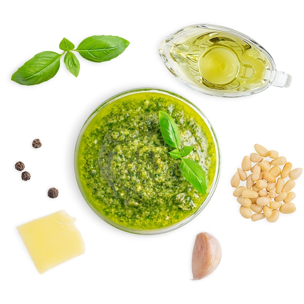 Draufsicht auf italienische Pesto-Sauce in Schüssel mit Basilikumblatt, Pinienkernen, Olivenöl und Parmesan auf Weiß