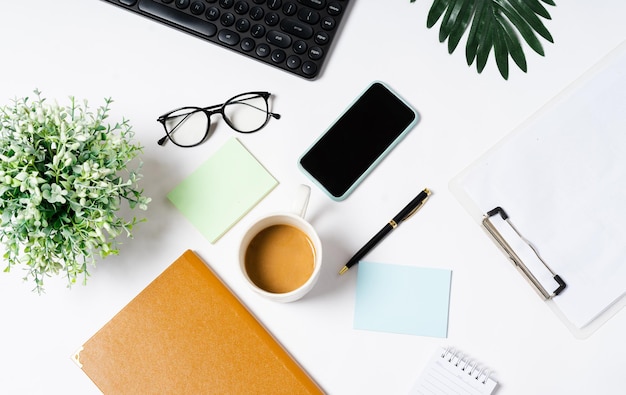 Draufsicht auf Kaffee, Buch, Notizbuch, Stift, Tastatur, Telefon auf weißem Hintergrund