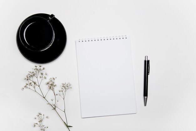 Draufsicht auf Kaffeetasse und Notizbuch mit Blumen auf weißem Hintergrund