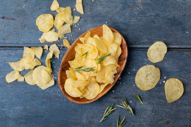 Foto draufsicht auf kartoffelchips in einer schüssel mit rosmarin und salz auf einem holztisch. unverändertes, ungesundes essen, snack, kräuter- und salzsnack.