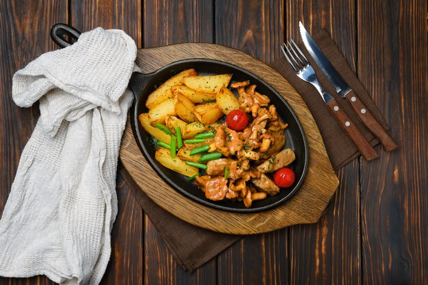 Draufsicht auf Kartoffelschnitze mit Pfifferlingen und Schweinefleisch in der gusseisernen Pfanne