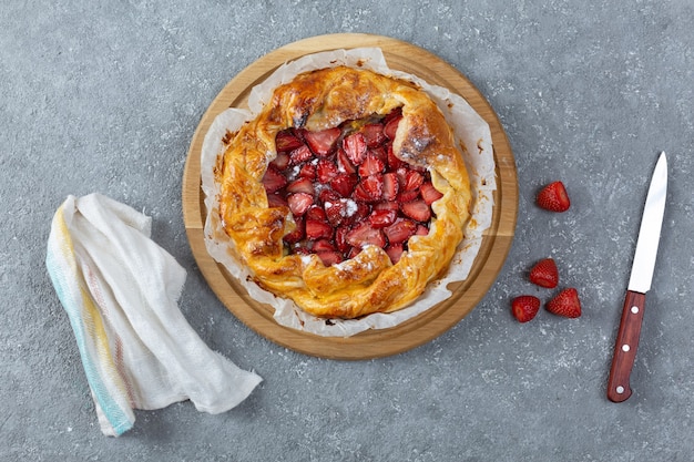 Draufsicht auf köstliche gebackene Torte mit Erdbeeren, Messer und Küchentuch auf hellgrauem Hintergrund gray