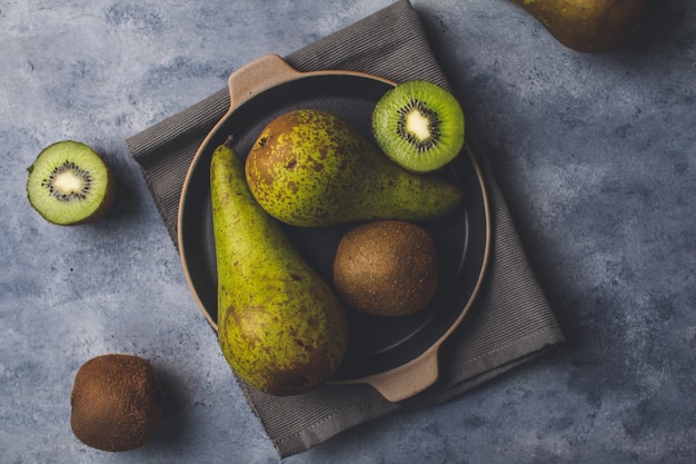 Draufsicht auf köstliche reife Kiwis und Birnen auf einem Tablett auf dem Tisch