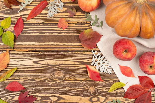 Foto draufsicht auf kürbisse und äpfel auf brauner holzoberfläche mit buntem herbstlaub herbstkonzept