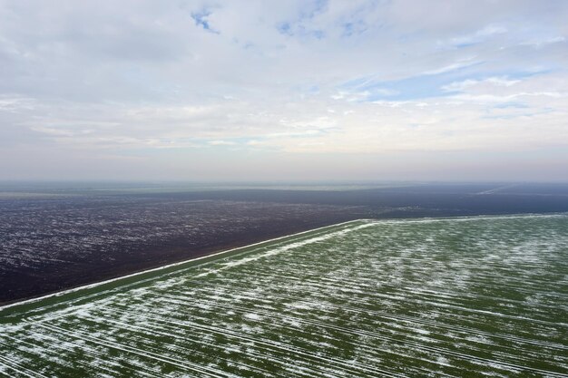 Draufsicht auf landwirtschaftliche grüne und braune Felder mit Schnee bedeckt.