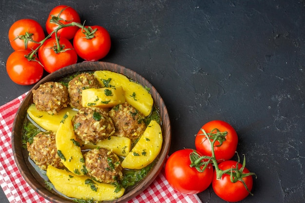 Draufsicht auf leckeres Abendessen mit Frikadellen Kartoffeln grün in einer braunen Schüssel auf rot gestreiften Handtuchtomaten auf schwarzem Hintergrund mit freiem Platz