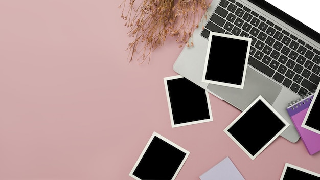 Draufsicht auf leere Fotorahmen, Laptop-Computer und getrockneten Blumenstrauß auf rosa Hintergrund
