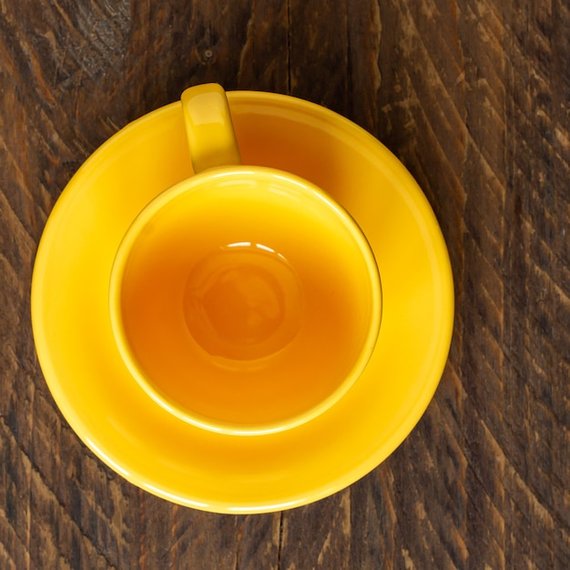Draufsicht auf leere gelbe Tasse und Untertasse auf rustikalem Holzboden. Küchengeschirr.