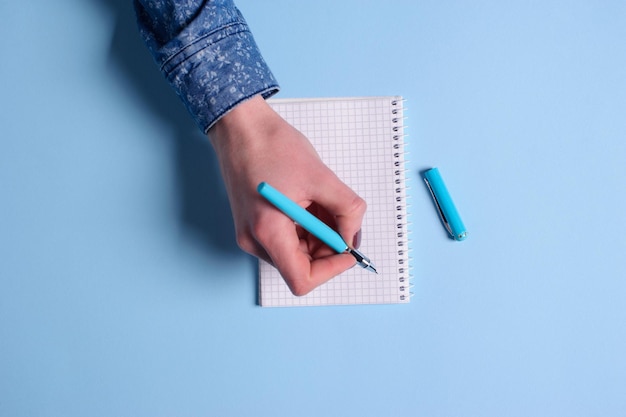 Draufsicht auf leeres Notizbuch mit Hand und Stift auf blauem Hintergrund