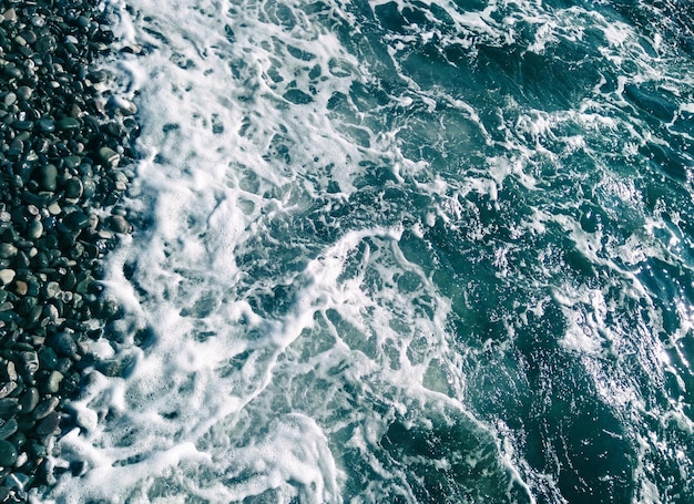 Draufsicht auf Meerwasser mit Schaum und Wellen und Kiesstrand Hintergrund