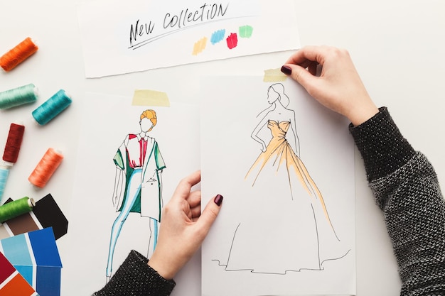 Draufsicht auf Modedesigner bei der Arbeit. Weibliche Hände, die mit Kleidungsskizze an ihrem Arbeitsplatz arbeiten, Kopienraum, Draufsicht. Neues Kollektionskonzept erstellen