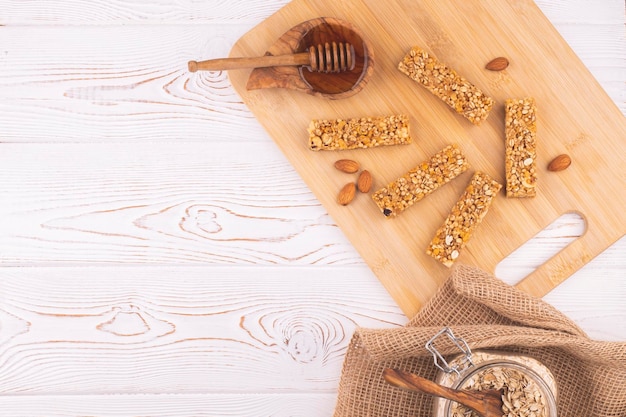 Draufsicht auf Müsliriegel mit Nüssen und Honig auf einem weißen Holztisch. Gesunder süßer Dessert-Snack