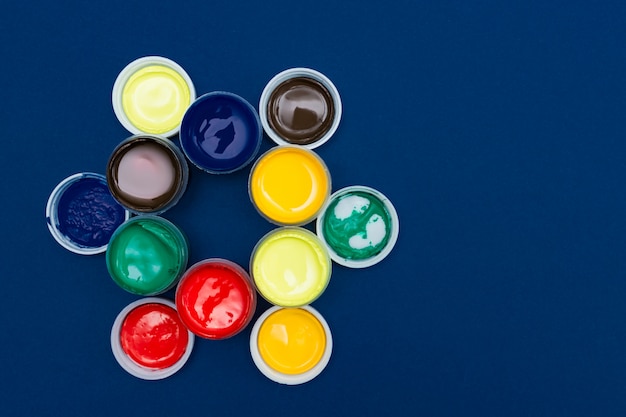 Draufsicht auf offene Acrylfarbdosen. Bunte Farben auf blauem Hintergrund mit Kopienraum