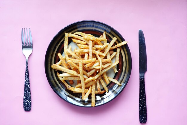 Draufsicht auf Pommes Frites auf einem Teller mit Besteck auf dem Tisch