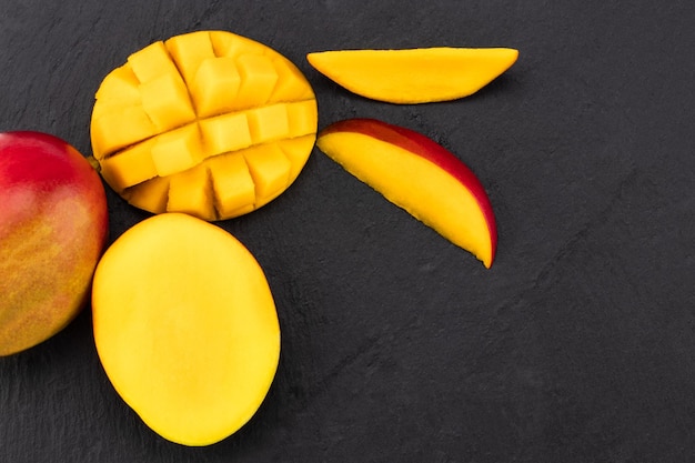 Foto draufsicht auf reife mango, halbiert und auf dunklem schiefer gewürfelt.