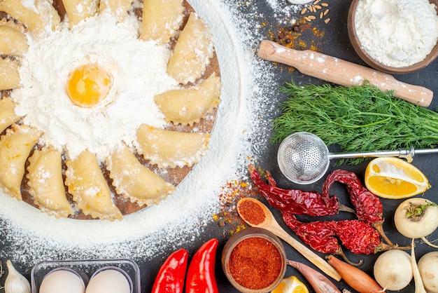 Draufsicht auf rohe Knödel auf braunem Tablett mit Mehl und Lebensmittel auf dunklem Farbtisch