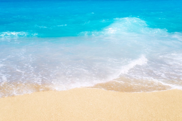 Draufsicht auf Sandstrand mit blauem türkisfarbenem Wasser und Wellen.
