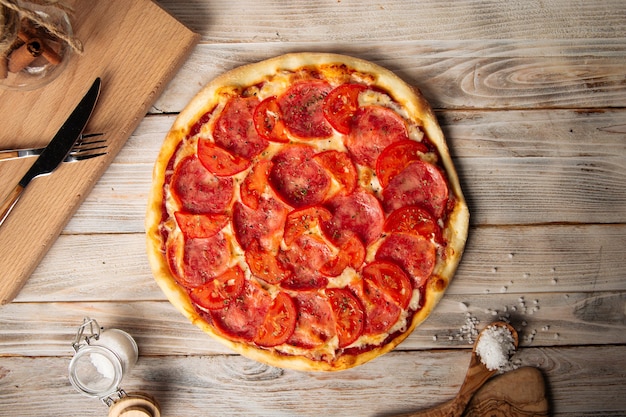 Draufsicht auf Schinkenpizza mit Tomate mit getrockneten Kräutern auf dem Holztisch